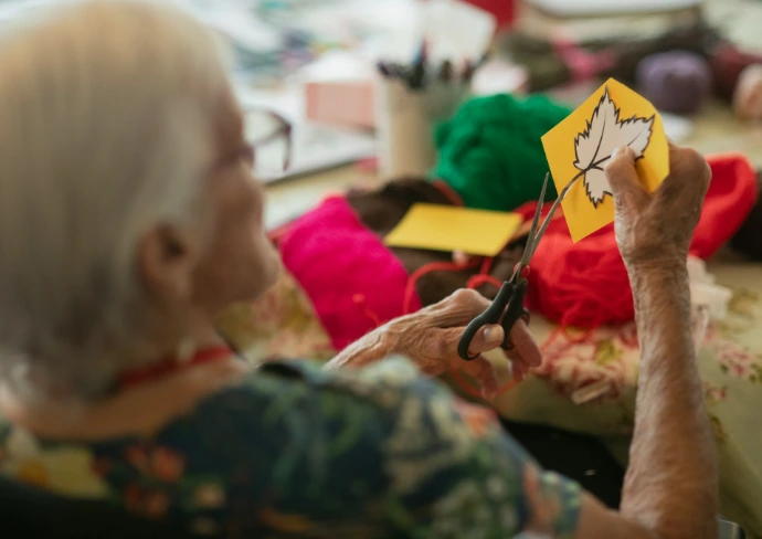 Elderly woman crafts autumn leaf decoration with scissors.
